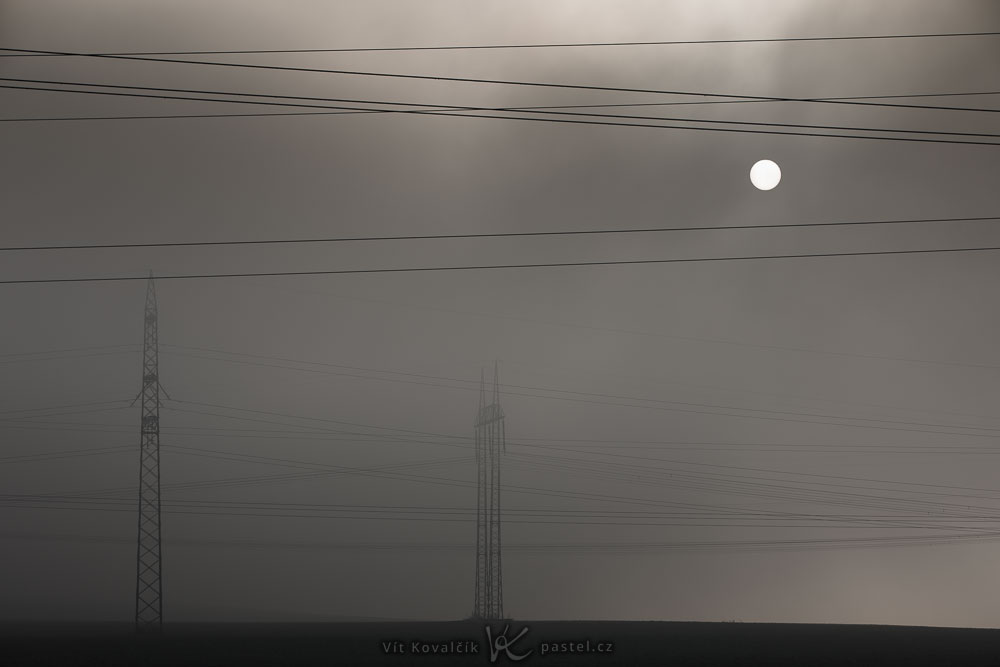 Landschaftsaufnahmen mit dem Teleobjektiv: Oberleitungsmasten im Nebel mit Sonnenlicht am Nachmittag.